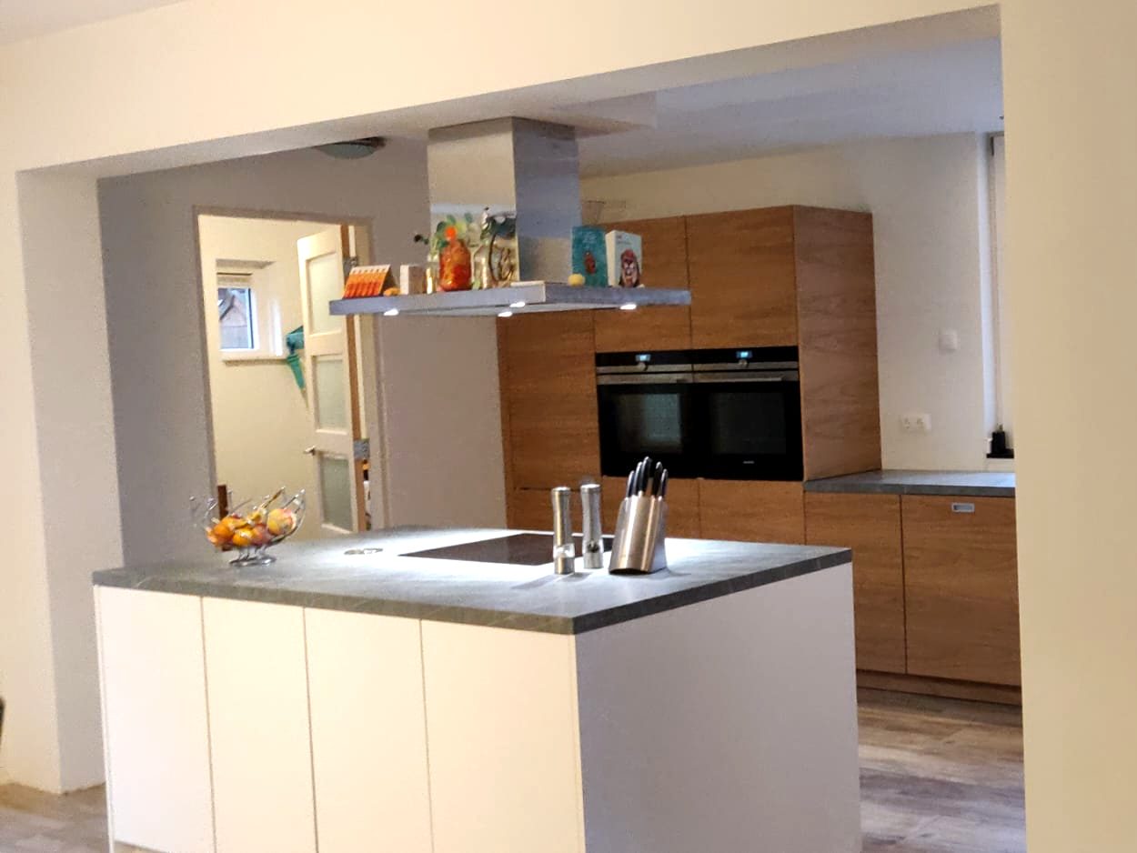 Nieuwe keuken met wit kookeiland en houten kastenwand met inbouwovens